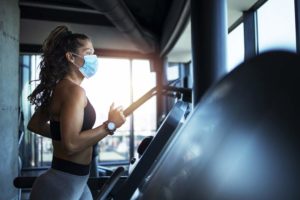 Sportswoman training on treadmill in gym and wearing face mask t