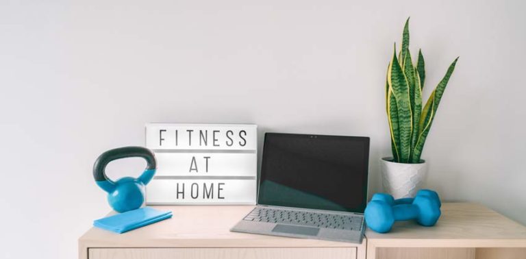 Fitness at home online exercise class on computer laptop with training weights and resistance band. Coronavirus COVID 19 Social distancing sign lightbox banner staying indoor while gyms are closed.