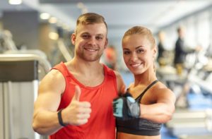 Smiling man and woman showing thumbs up in gym